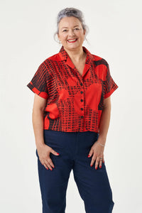 Woman wearing the Libby Blouse sewing pattern from Sew Over It on The Fold Line. A shirt pattern made in rayon, viscose, or crepe fabric, featuring a loose fit, button-up front, notched collar, partial collar stand, unlined yoke with a gently gathered back, short grown-on cuffed sleeves, and a cropped hem.