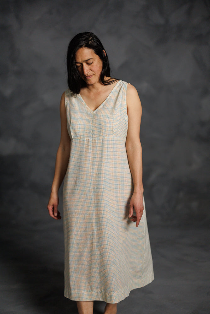Woman wearing the Lilian Slip Dress sewing pattern from Merchant & Mills on The Fold Line. A sleeveless slip dress or nightdress pattern made in cotton lawn or voile, cotton poplin, tencel, Indian handlooms, or cotton double gauze fabric, featuring a V-neck, gathered shoulders, empire line, and midi length.