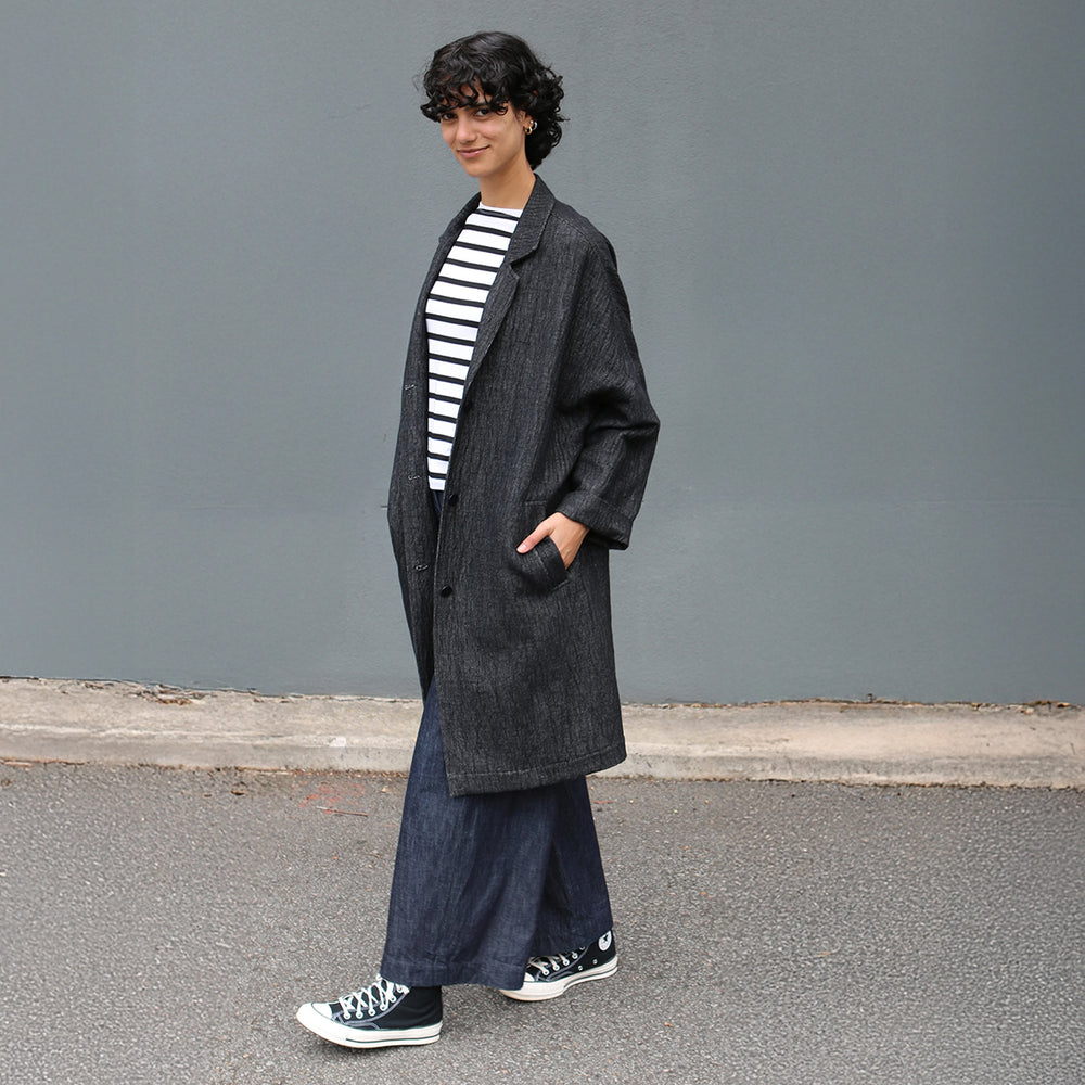 Woman wearing the Lisbon Jacket sewing pattern from Tessuti Fabrics on The Fold Line. An unlined jacket pattern made in linen or linen blends, wool blends, corduroy, or wool crepe fabric, featuring a notched collar, dropped shoulders, long tapered sleeves which can be cuffed, button front, welt pockets, and knee length.