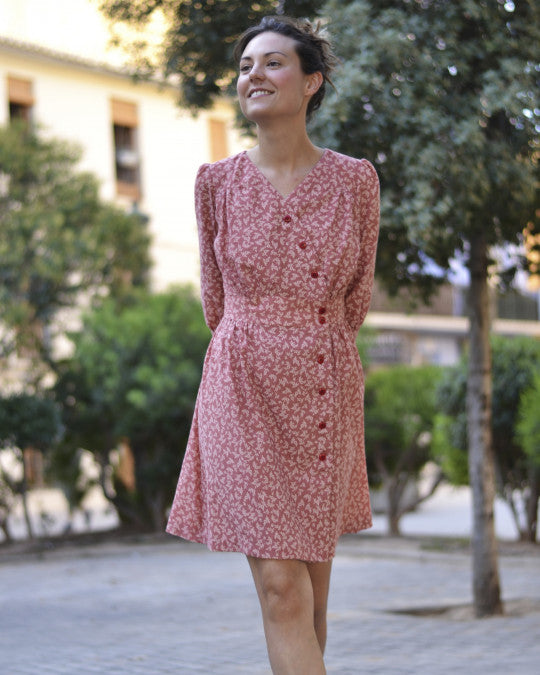 Woman wearing the Lliria Dress sewing pattern from Pauline Alice on The Fold Line. A dress pattern made in cotton lawn, linen, rayon, silk, or crepe fabric, featuring a V-neck, gathered bodice and skirt, shaped waistband, asymmetric button closure, elbow length sleeves, and above-the-knee skirt.