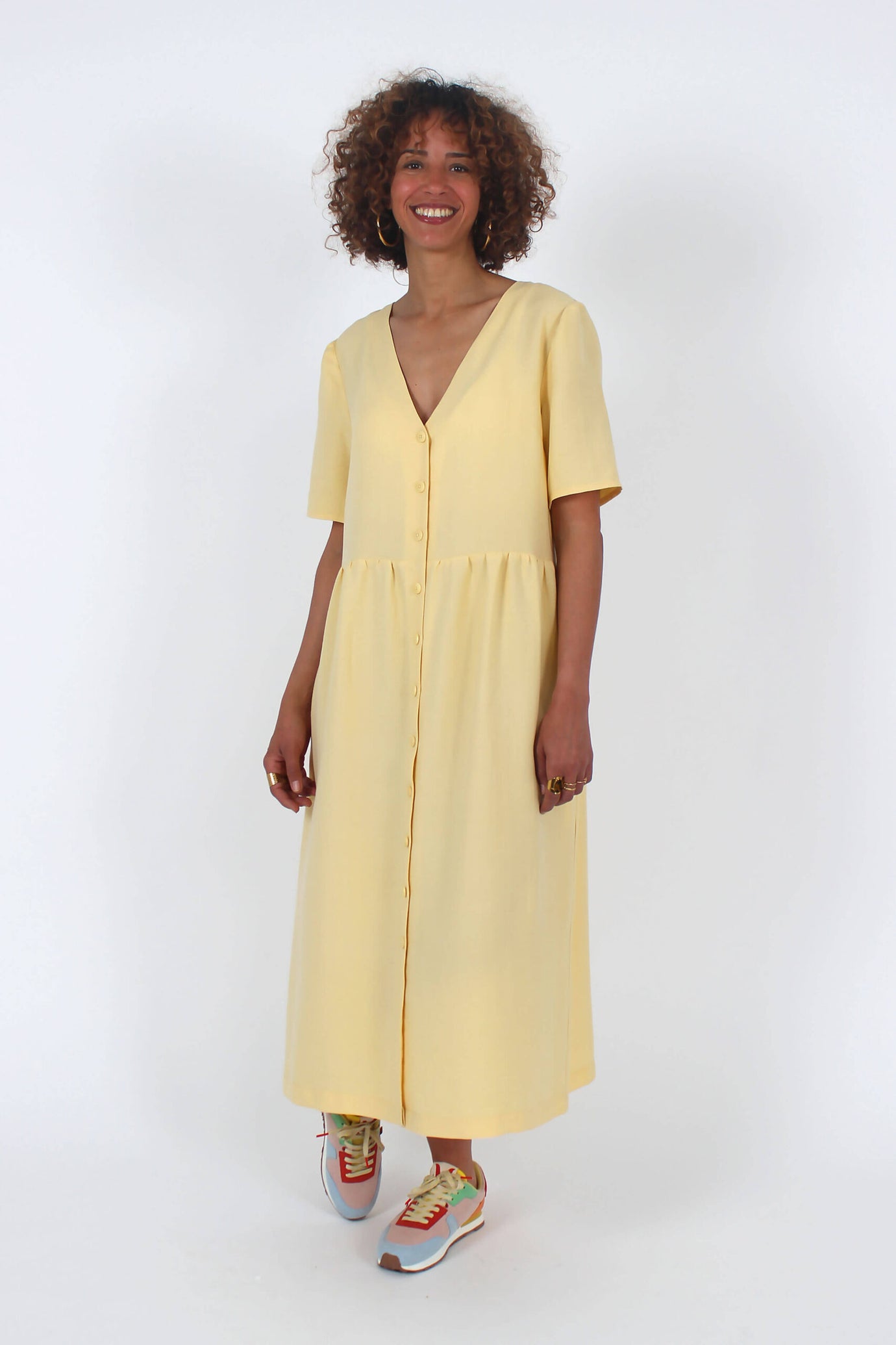 Woman wearing the Lotus Dress sewing pattern from I AM Patterns on The Fold Line. A dress pattern made in poplin, viscose, tencel, Tana lawn, chambray, light crepe, lightweight denim, silk, linen, or washed cotton fabric, featuring a deep V-neck, short sleeves, button front, gathered skirt, and side pockets.