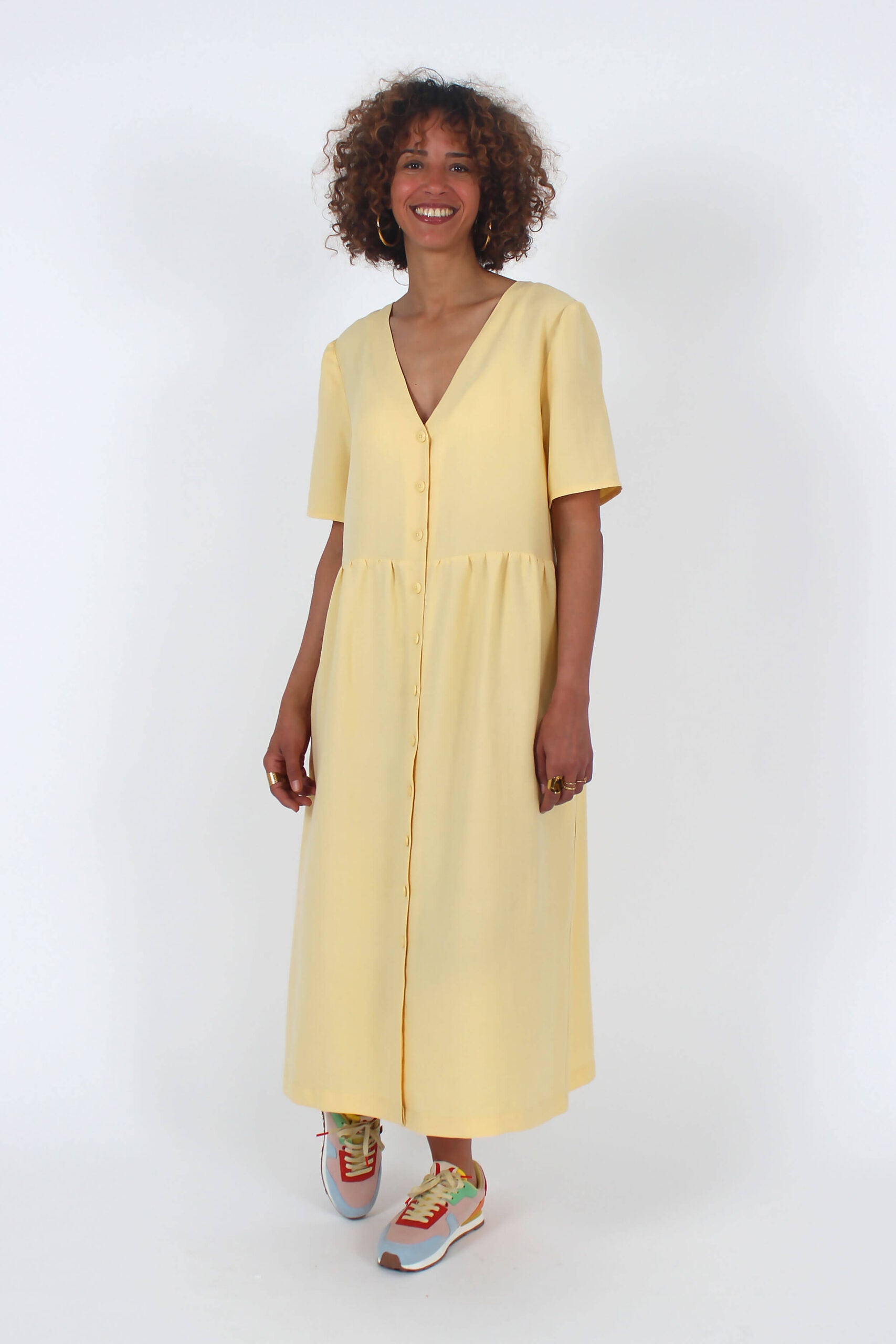 Woman wearing the Lotus Dress sewing pattern from I AM Patterns on The Fold Line. A dress pattern made in poplin, viscose, tencel, Tana lawn, chambray, light crepe, lightweight denim, silk, linen, or washed cotton fabric, featuring a deep V-neck, short sleeves, button front, gathered skirt, and side pockets.