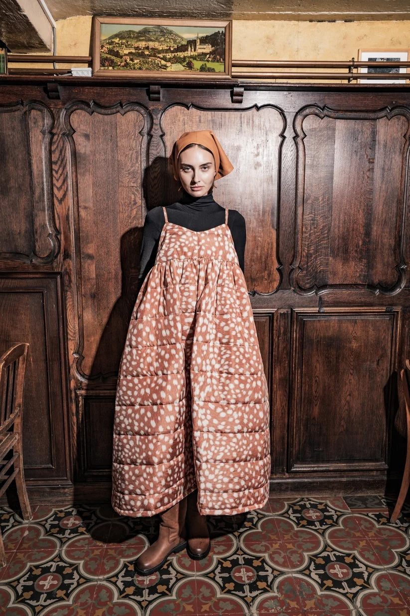 Woman wearing the Louisa Dress sewing pattern from Fibre Mood on The Fold Line. A sleeveless dress pattern made in cotton, linen, poplin, light jacquard, or quilted fabric, featuring narrow shoulder straps, gathers at the front of the skirt and a pleat at the back, an oversized bow at the back, pockets, and midi length.