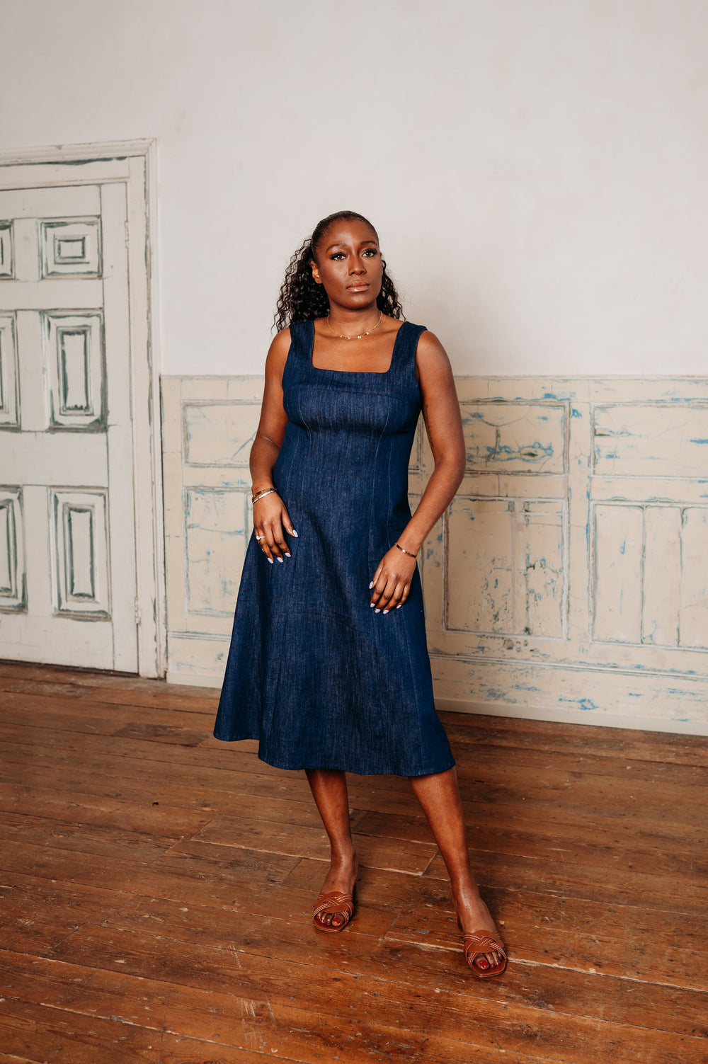 Woman wearing the Lucia Dress sewing pattern from NH Patterns on The Fold Line. A sleeveless dress pattern made in cotton shirting, cotton twill, lightweight denim, chambray, linen, linen blends, tencel, or suiting fabric, featuring princess seams, a square neckline, low back, and midi length.