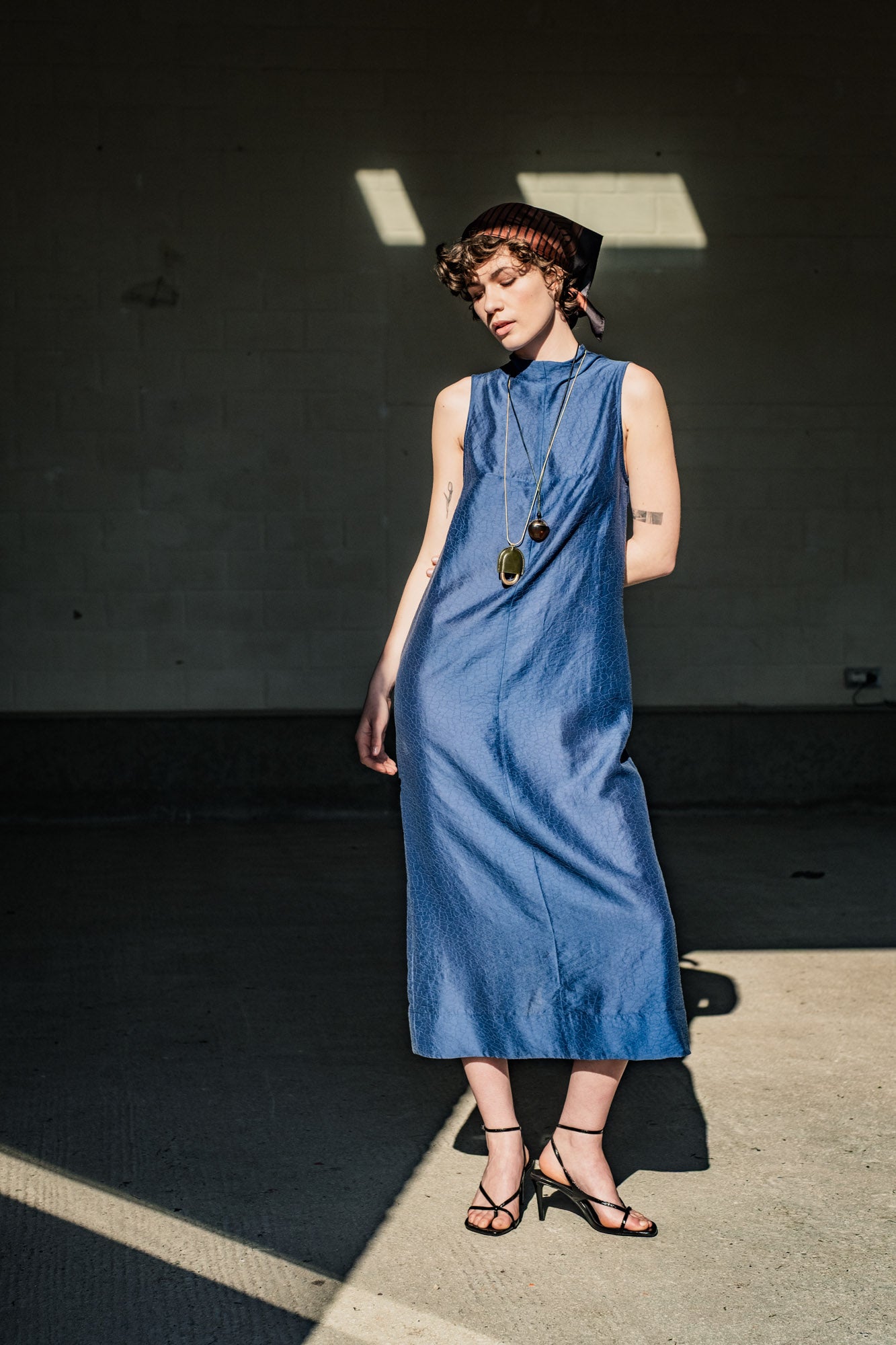Woman wearing the Lumen Dress sewing pattern from Fibre Mood on The Fold Line. A sleeveless dress pattern made in viscose, silk, lyocell, seersucker, crepe, chambray, double gauze, or tulle fabric, featuring a slightly fitted cut, high neckline, back slit, and midi length.