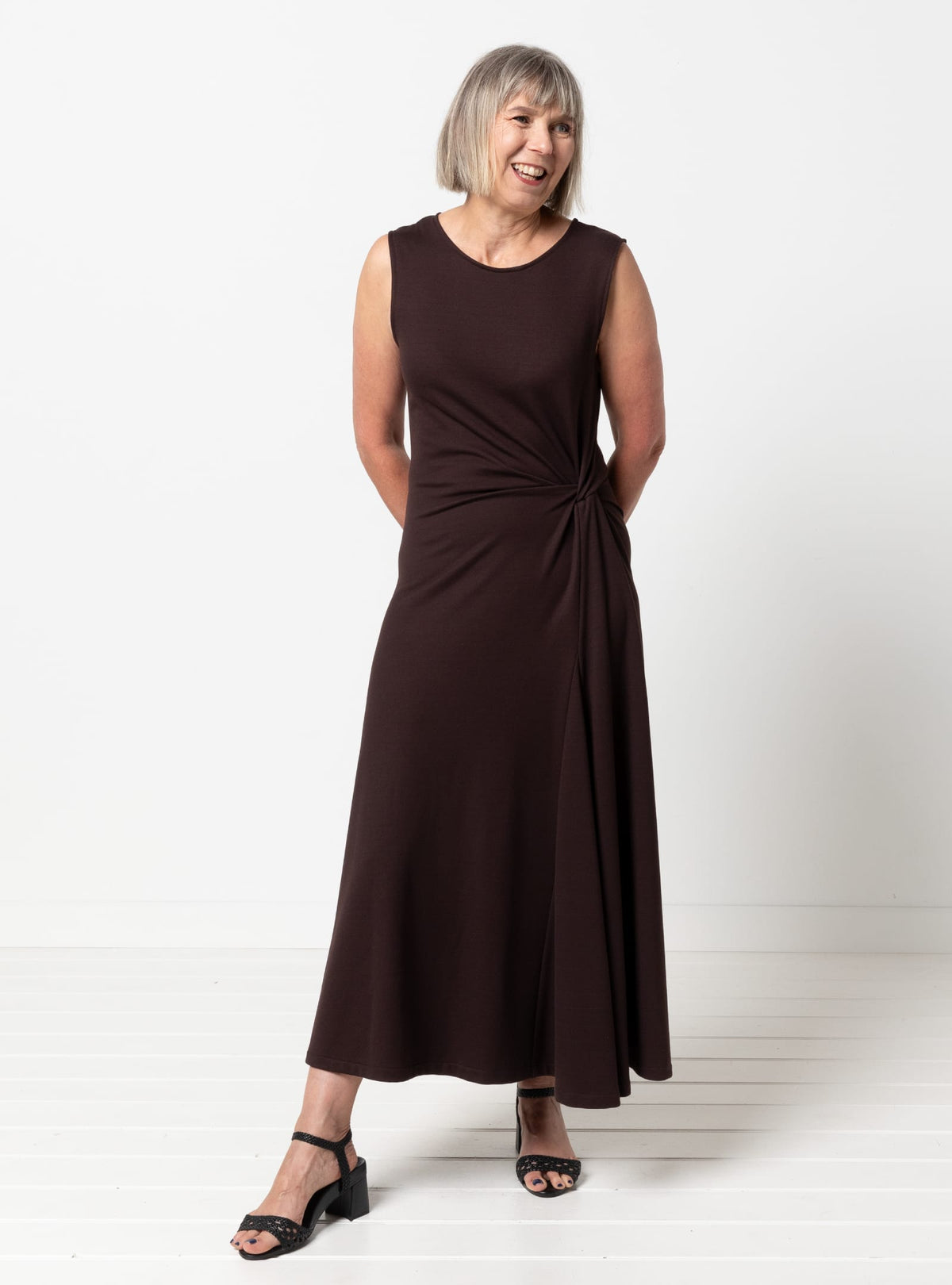 Woman wearing the Lumi Knit Dress sewing pattern from Style Arc on The Fold Line. A sleeveless dress pattern made in cotton spandex, scuba, ponte, interlock knit, or rib knit fabric, featuring a subtle A-line shape, round neckline, twisted detail at the waist, and midi length.