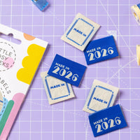 The 'Made in 2026' woven labels from Little Rosy Cheeks on The Fold Line. The pack includes 6 embossed labels with an ecru or blue background, ready to be sewn into your handmade clothes.