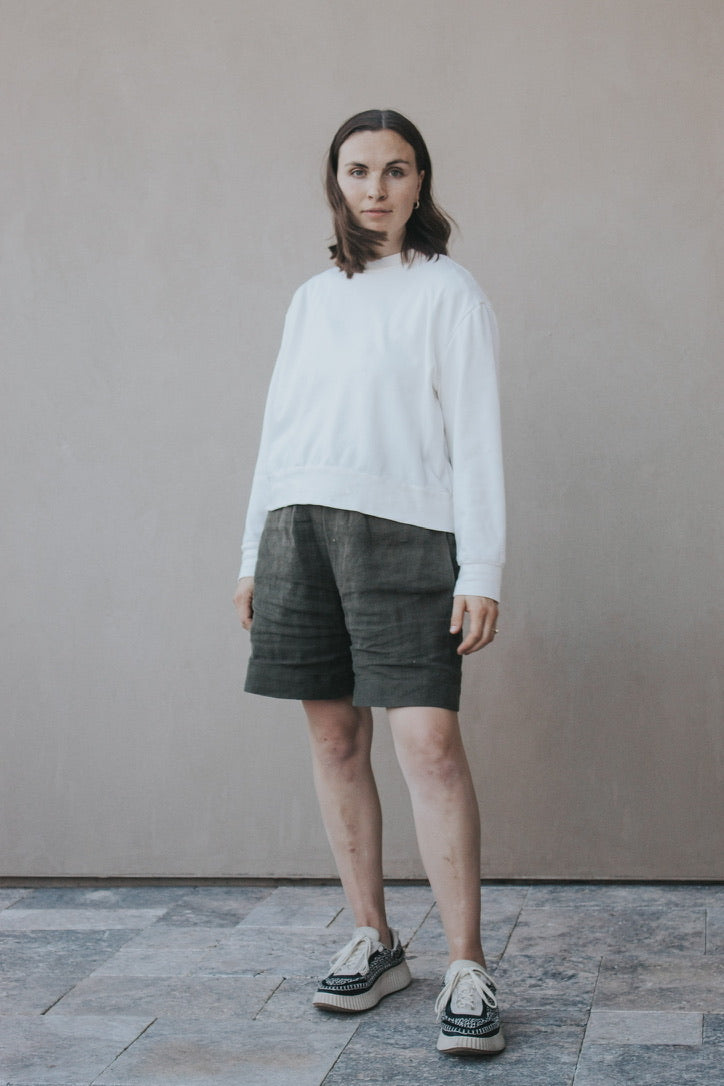 Woman wearing the Madeline Sweatshirt sewing pattern from Madswick on The Fold Line. A sweatshirt pattern made in knit fabric such as French terry, ponte, rib, jersey, fleece, modal, or waffle fabric, featuring a round neck, slightly dropped shoulders, long sleeves with wrist cuffs, and a wide hem band.