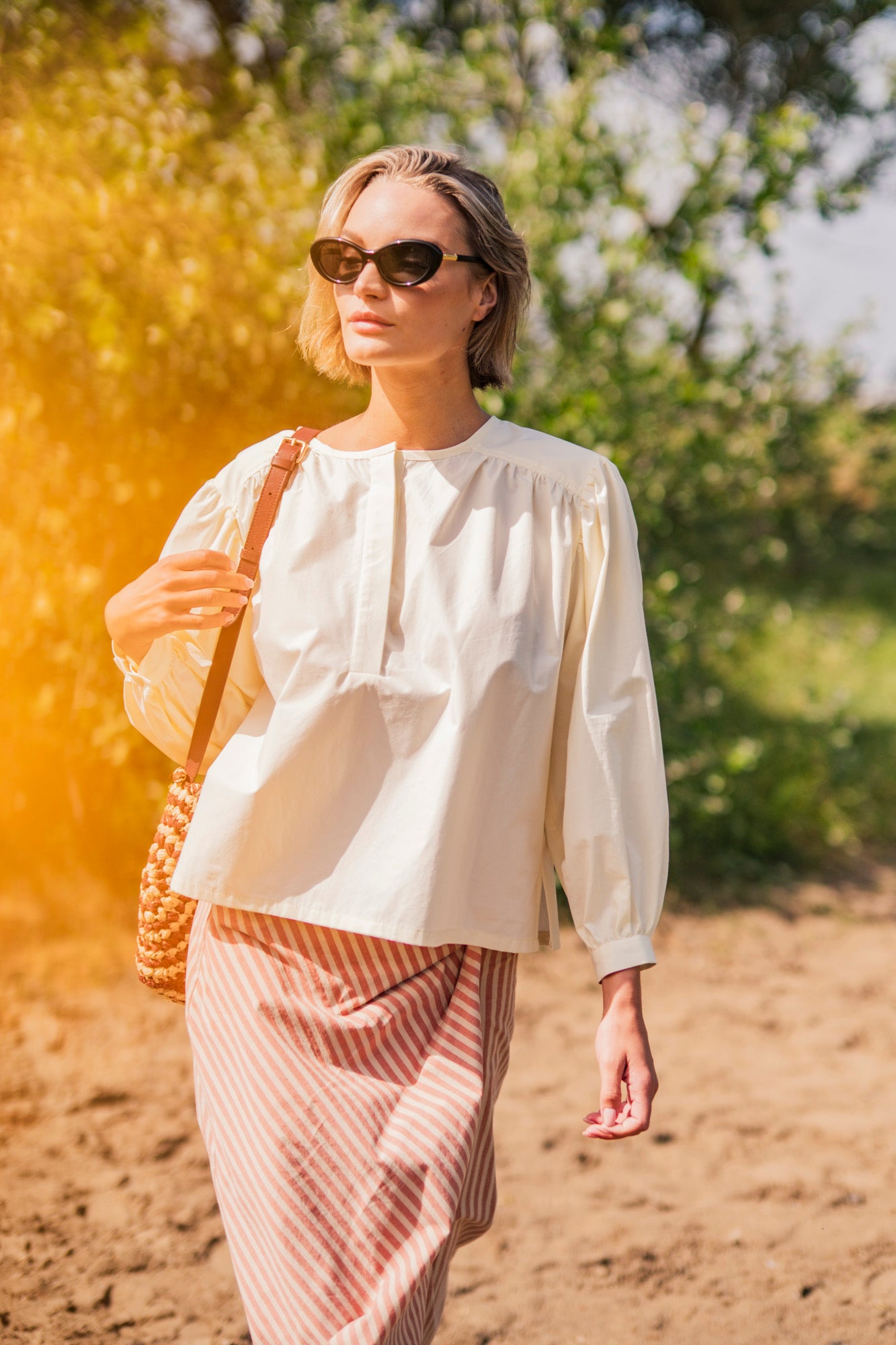 Woman wearing the Maris Top sewing pattern from Fibre Mood on The Fold Line. A blouse pattern made in poplin, cotton sateen, nylon, taffeta, crepe, viscose satin, chambray, muslin, linen, seersucker, or double gauze fabric, featuring a round neckline, hidden polo placket, gathers at the front and back, and voluminous gathered sleeves.