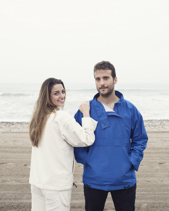 Man and woman wearing the Marítims Pullover sewing pattern from Pauline Alice on The Fold Line. A lined top pattern made in cotton canvas, denim, gabardine, corduroy, or nylon fabric, featuring a high collar with snaps, zipped opening offset to the side, large front pocket, interior pocket, cuffed sleeves, and adjustable hem with drawstrings. 