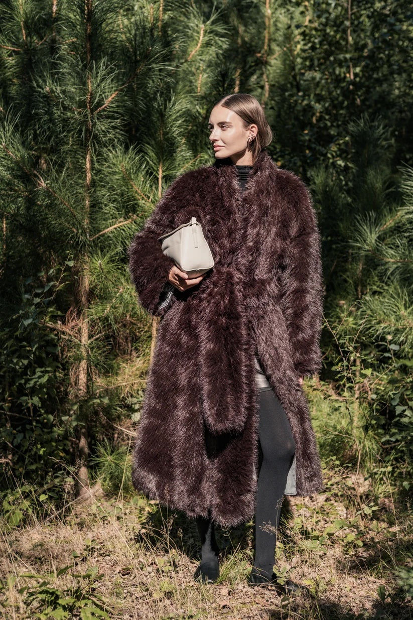 Woman wearing the Marwi Coat sewing pattern from Fibre Mood on The Fold Line. A reversible coat pattern made in faux fur, teddy, or wool fabric, featuring a shawl collar, tie belt, pockets, and calf length.