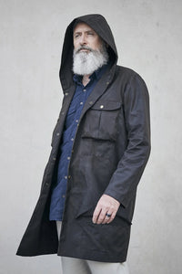 Man wearing the Men's Akerfeldt Coat sewing pattern from Elbe Textiles on The Fold Line. A coat pattern made in canvas, waxed canvas, oil cloth, rigid denim, corduroy, or duck cotton fabric, featuring a hood, chest pockets with flaps, and hip pockets.