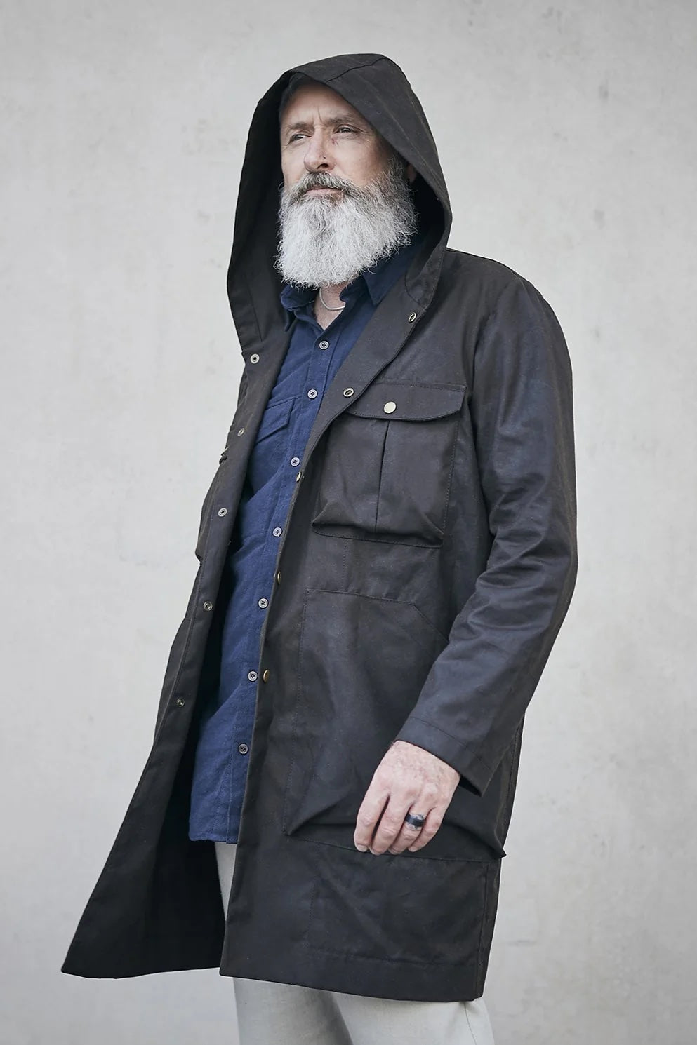 Man wearing the Men's Akerfeldt Coat sewing pattern from Elbe Textiles on The Fold Line. A coat pattern made in canvas, waxed canvas, oil cloth, rigid denim, corduroy, or duck cotton fabric, featuring a hood, chest pockets with flaps, and hip pockets.