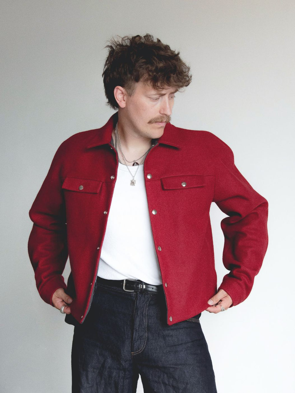 Man wearing the Men’s Jordy Jacket sewing pattern from Notches on The Fold Line. An unlined jacket pattern made in denim, corduroy, or cotton canvas fabric, featuring a raglan yoke, collar, cuffed sleeves, snap front, and pockets.