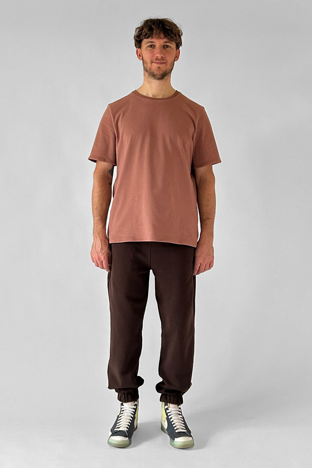 Man wearing the Men's Mowgli Joggers sewing pattern from I AM Patterns on The Fold Line. A joggers pattern made in jersey, fleece, or French terry fabric, featuring a relaxed fit, elasticated waist, drawstring, pockets, and elasticated cuffs.