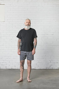 Man wearing the Men's Trigg Shorts sewing pattern from Elbe Textiles on The Fold Line. A shorts pattern made in tencel, chambray cotton, denim, linen, or boardshort fabric, featuring an elasticated waistband with a drawstring, side pockets, and back patch pockets.