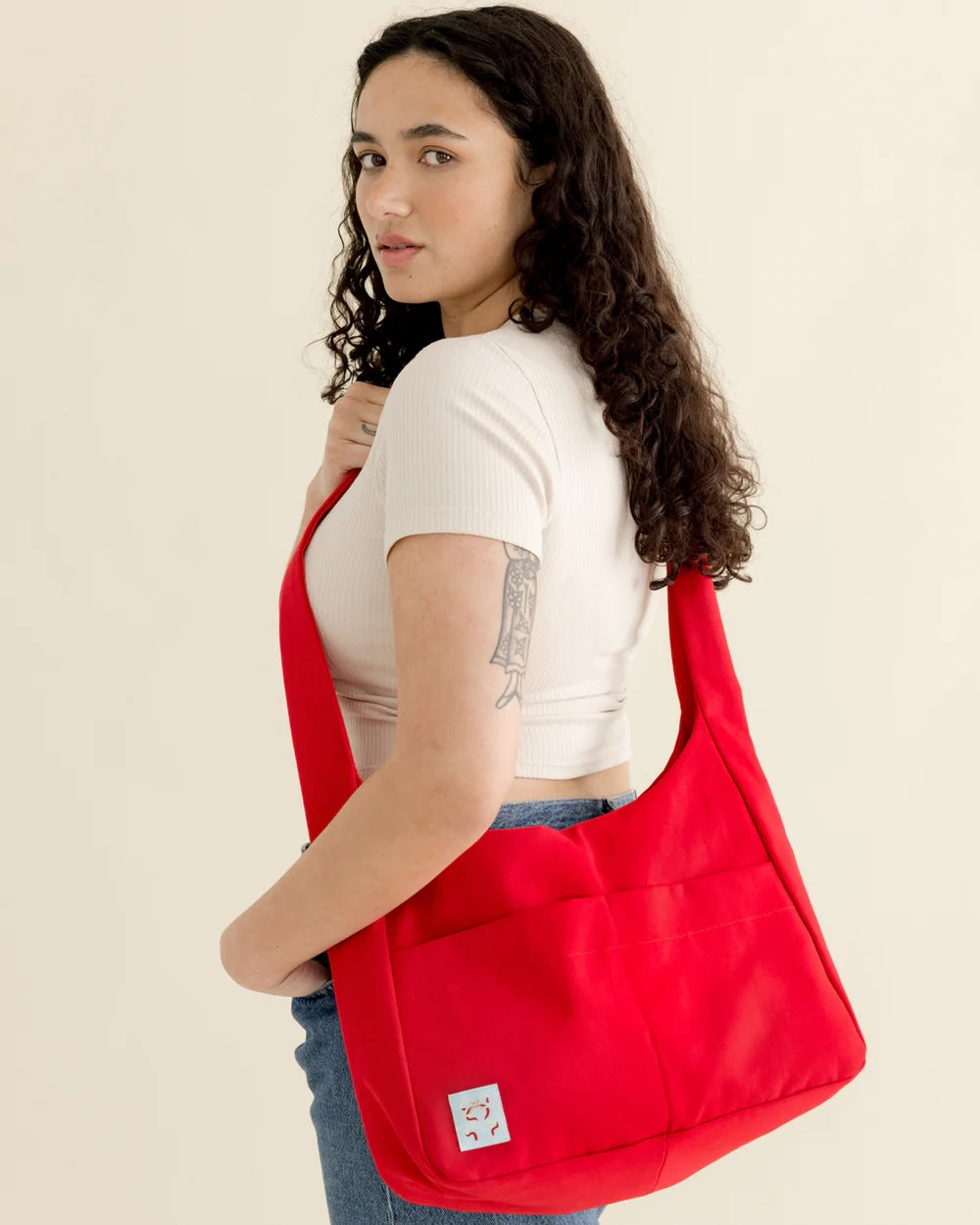 Woman wearing the Mia Messenger Bag sewing pattern from BF Patterns on The Fold Line. A bag pattern made in denim, canvas, twill, heavyweight nylon, ripstop, faux leather, or vinyl fabric, featuring a top zipper, magnetic snap closure, two front pockets, and a full lining with a zippered pocket and device pocket.