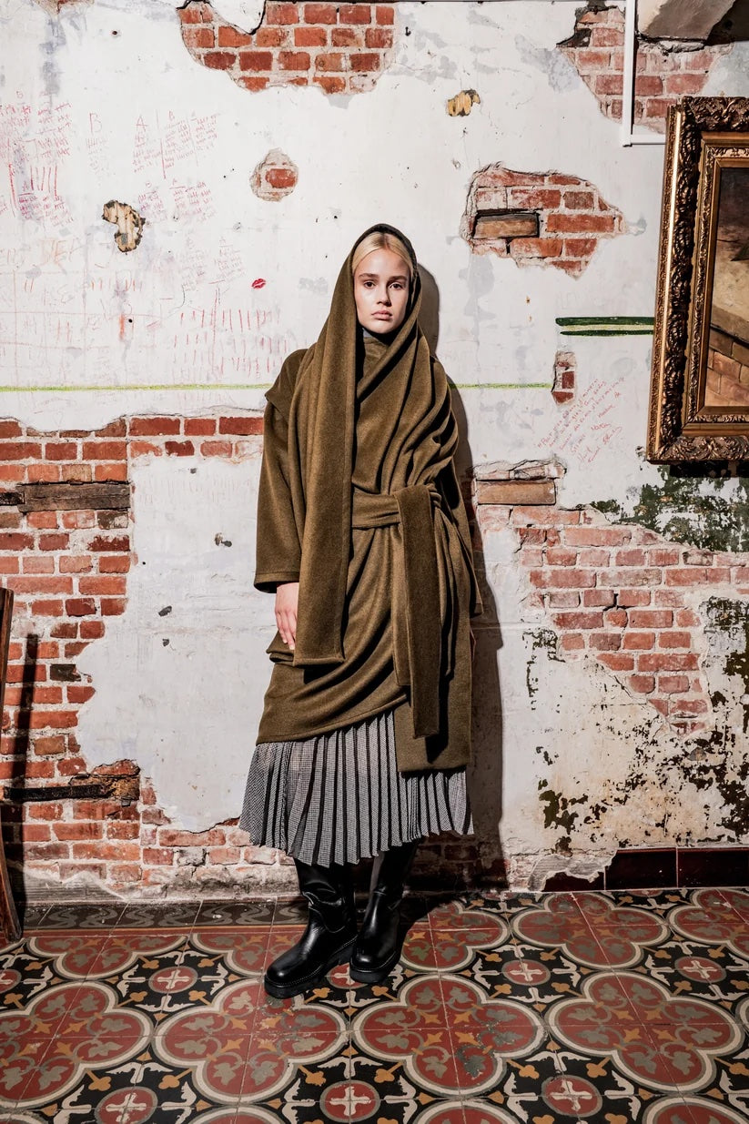 Woman wearing the Mingus Coat sewing pattern from Fibre Mood on The Fold Line. A coat pattern made in wool, wool blend, or coating fabric, featuring an integrated scarf, tie belt, and detachable sleeves.