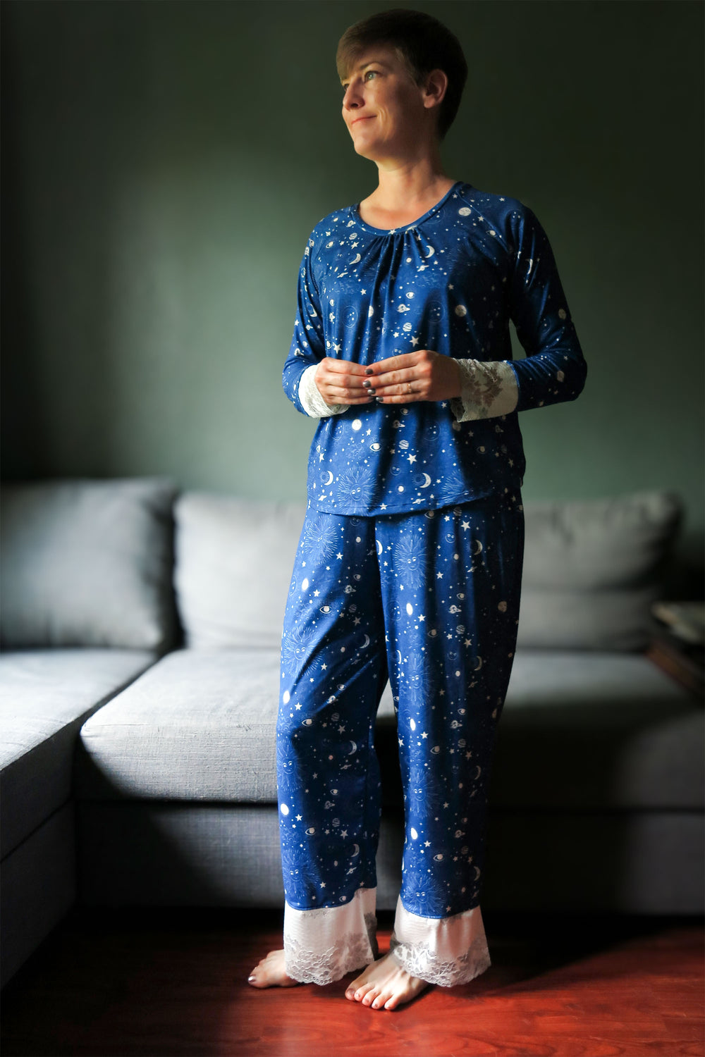 Woman wearing the Mona Sira Pajamas sewing pattern from Primrose Dawn on The Fold Line. A nightwear pattern made in knit fabric for the top and knit or linen, rayon challis, crinkle gauze, cotton lawn, or satin fabric for the trousers, featuring a top with a round neckline, neckline gathers, and long raglan sleeves with lace cuffs, and elastic waist trousers with lace cuffs.