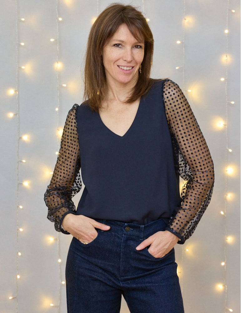 Woman wearing the Muse Blouse sewing pattern from Atelier Scämmit on The Fold Line. A top pattern made in crepe, poplin, jacquard, cotton, silk, or linen fabric, featuring a V-neckline, long sleeves, and button back.