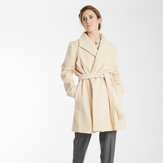 Woman wearing the Nadia Coat sewing pattern from Coralie Bijasson on The Fold Line. A wrap coat pattern made in wool fabric, featuring a wide shawl collar, side seam pockets, and removable tie belt.