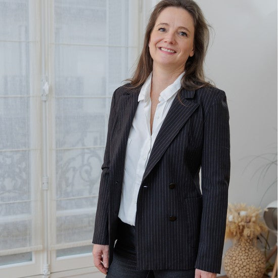 Woman wearing the Naelle Blazer sewing pattern from Coralie Bijasson on The Fold Line. A jacket pattern made in cotton satin, cotton piqué, wool, denim, gabardine, jacquard, or corduroy fabric, featuring notched lapels, a double-breasted front, and patch pockets.