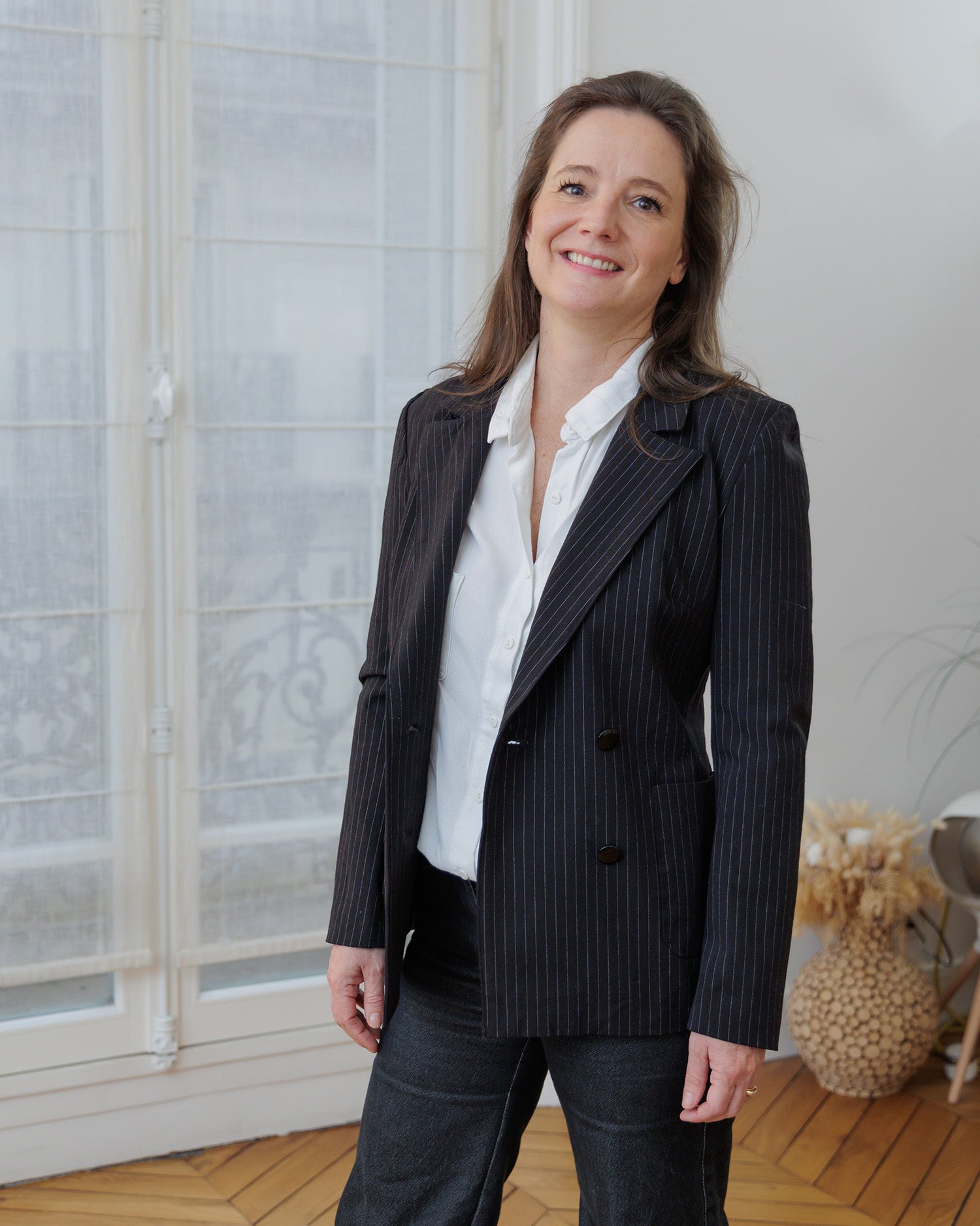 Woman wearing the Naelle Blazer sewing pattern from Coralie Bijasson on The Fold Line. A jacket pattern made in cotton satin, cotton piqué, wool, denim, gabardine, jacquard, or corduroy fabric, featuring notched lapels, a double-breasted front, and patch pockets.