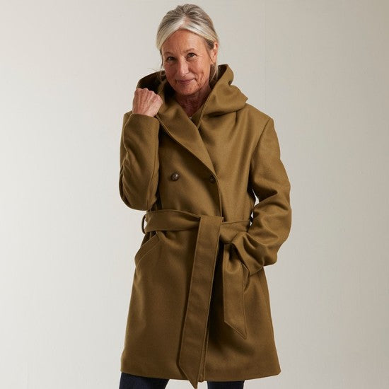 Woman wearing the Namasté Coat sewing pattern from Coralie Bijasson on The Fold Line. A lined coat pattern made in wool, denim, or jacquard fabric, featuring an oversized hood, double-breasted front, welt pockets, tie belt, and mid-thigh length.