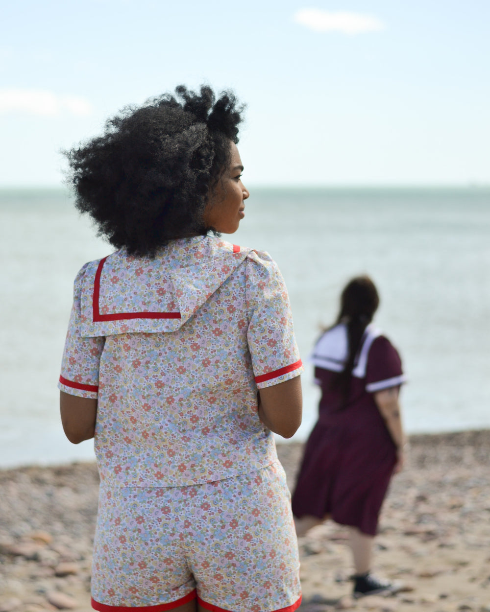 Women wearing the Nautic Set sewing pattern from Pauline Alice on The Fold Line. A blouse, shorts, and skirt pattern set made in cotton poplin or lawn, linen, chambray, viscose, or broderie anglaise fabric, featuring a button front blouse with a sailor collar and short sleeves, and shorts and skirt with an elasticated paper bag waist.