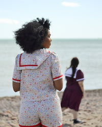 Women wearing the Nautic Set sewing pattern from Pauline Alice on The Fold Line. A blouse, shorts, and skirt pattern set made in cotton poplin or lawn, linen, chambray, viscose, or broderie anglaise fabric, featuring a button front blouse with a sailor collar and short sleeves, and shorts and skirt with an elasticated paper bag waist.