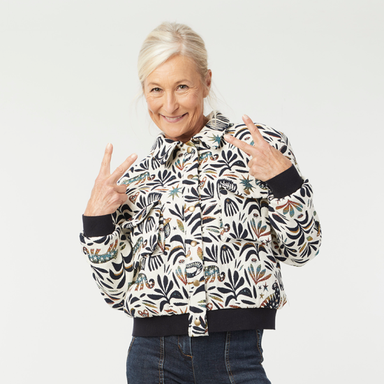 Woman wearing the Nessa Jacket sewing pattern from Coralie Bijasson on The Fold Line. A lined jacket pattern made in jacquard, wool, denim, gabardine, cotton satin, or lightweight damask fabric, featuring a collar, snap front closure, gusset chest pockets, side pockets, rib knit waistband and cuffs, and cropped length.