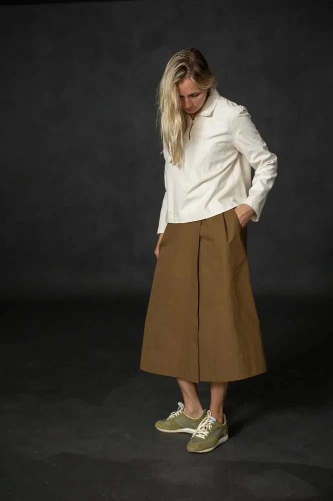 Woman wearing the Nevis Skirt sewing pattern from Merchant & Mills on The Fold Line. A wrap skirt pattern made in cotton canvas, twill, corduroy, wool, or denim fabric, featuring a high waistband with buttons, pockets, and midi length.