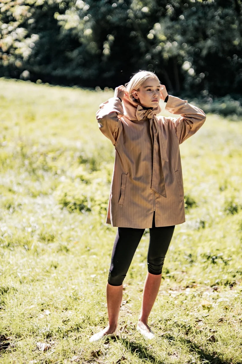 Woman wearing the Nigel Jacket sewing pattern from Fibre Mood on The Fold Line. A jacket pattern made in gabardine, twill, canvas, wool, wool blend, or technical fabric, featuring a relaxed fit, hood that extends into ties, front zip, and pockets.