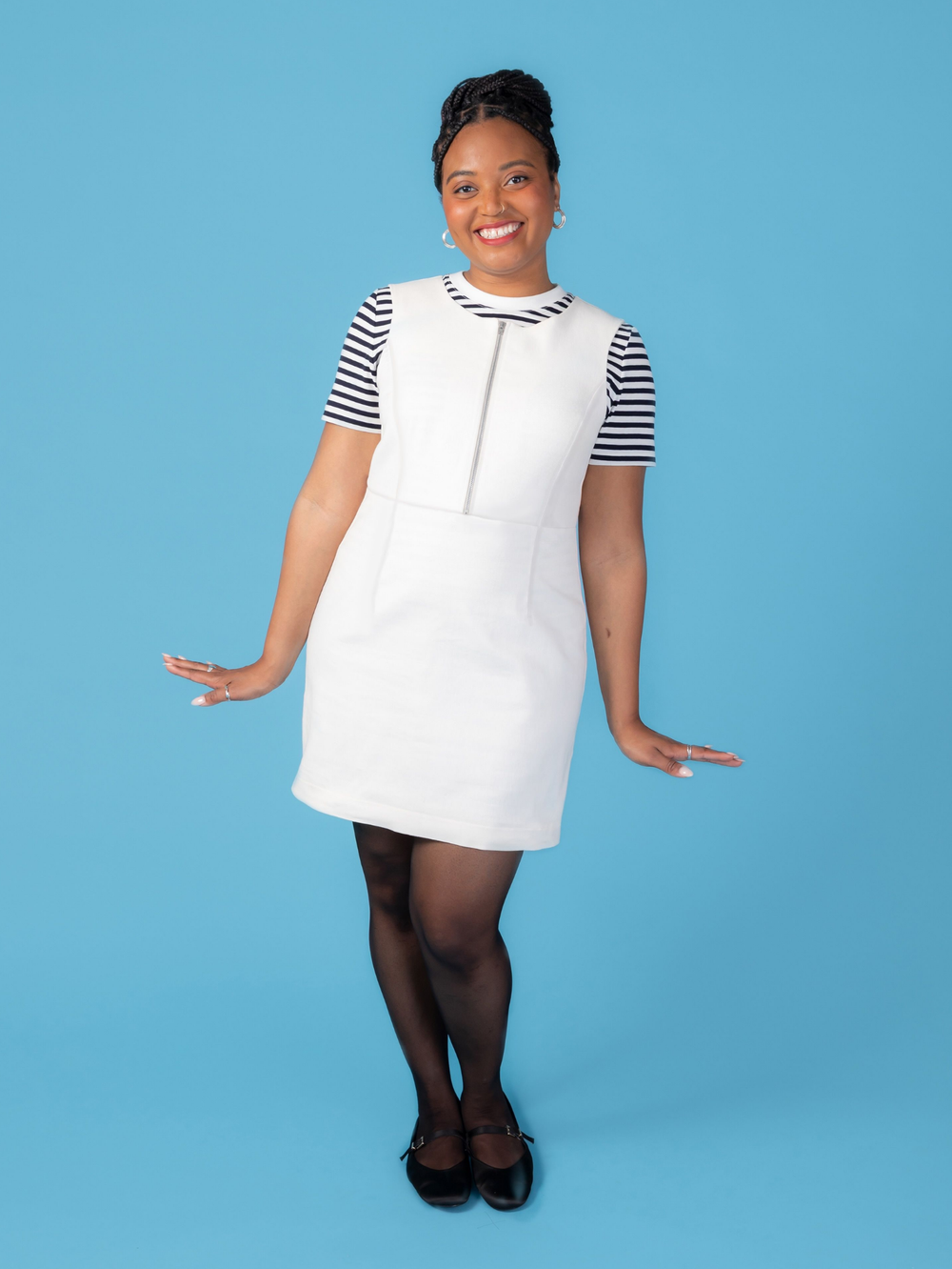 Woman wearing the Noa Pinafore sewing pattern from Tilly and the Buttons on The Fold Line. A sleeveless dress pattern made in denim, corduroy, twill, jacquard, or wool suiting fabric, featuring a round neck, princess seams, high waistline, exposed zip front opening, and mini length.