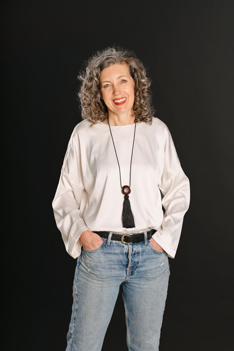 Woman wearing the Norwood Blouse sewing pattern from Liesl + Co on The Fold Line. A top pattern made in satin, lawn, linen, or crepe fabric, featuring an oversized fit, round neckline, dropped shoulder, two-piece long sleeve, and keyhole opening at the back.