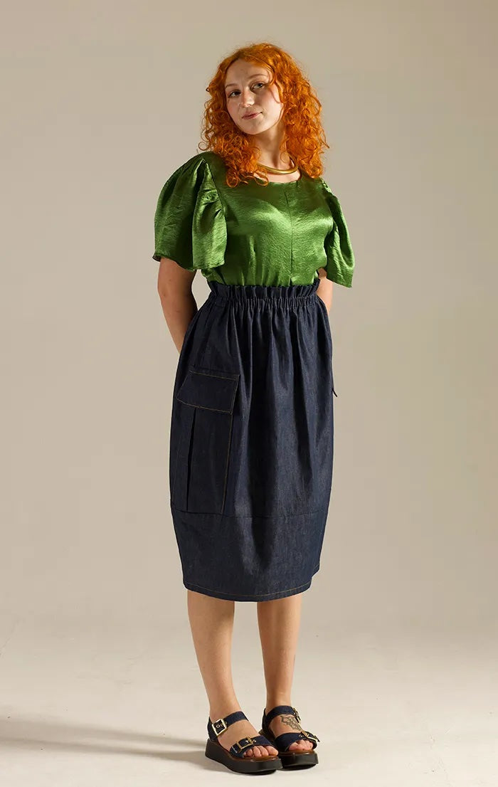 Woman wearing the Nox Skirt sewing pattern from Sew Different on The Fold Line. A skirt pattern made in denim, cotton, corduroy, linen, tweed, or wool fabric, featuring an elasticated paperbag waist, barrel shape, large cargo pockets, and knee length.