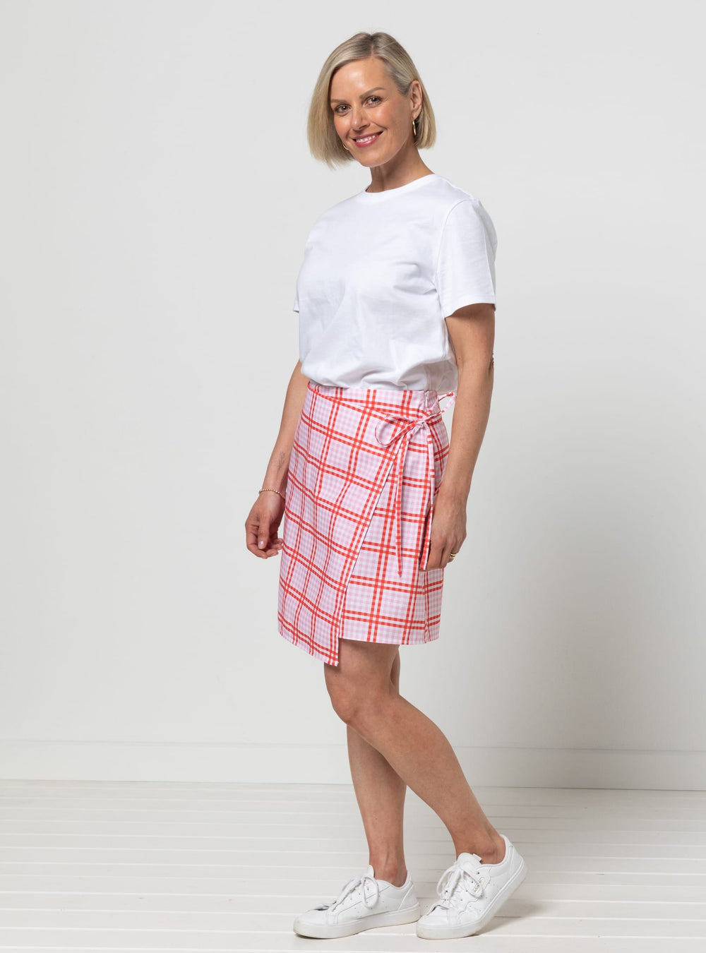Woman wearing the Octavia Woven Wrap Skirt sewing pattern from Style Arc on The Fold Line. A wrap skirt pattern made in gabardine, denim, heavy linen, cotton drill, corduroy, boiled wool, tweed wool, PU (polyurethane), leather, or suede fabric, featuring a wrap front with ties, asymmetrical front, and mini length.