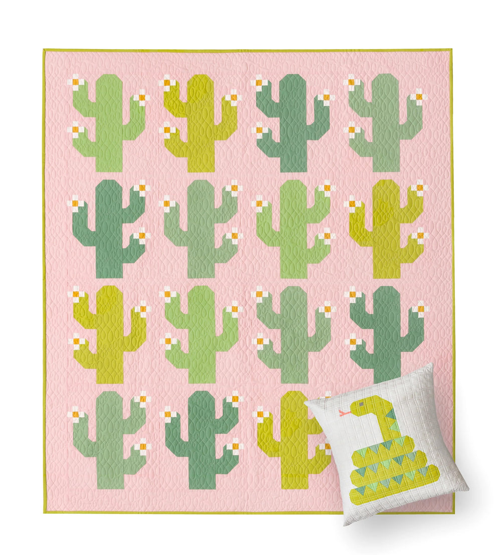 The Oh My Cacti Quilt sewing pattern from Pen + Paper Patterns on The Fold Line. A quilt pattern made in quilting cotton fabric, featuring cacti with flowers on a plain background and a bonus throw pillow with a snake design.