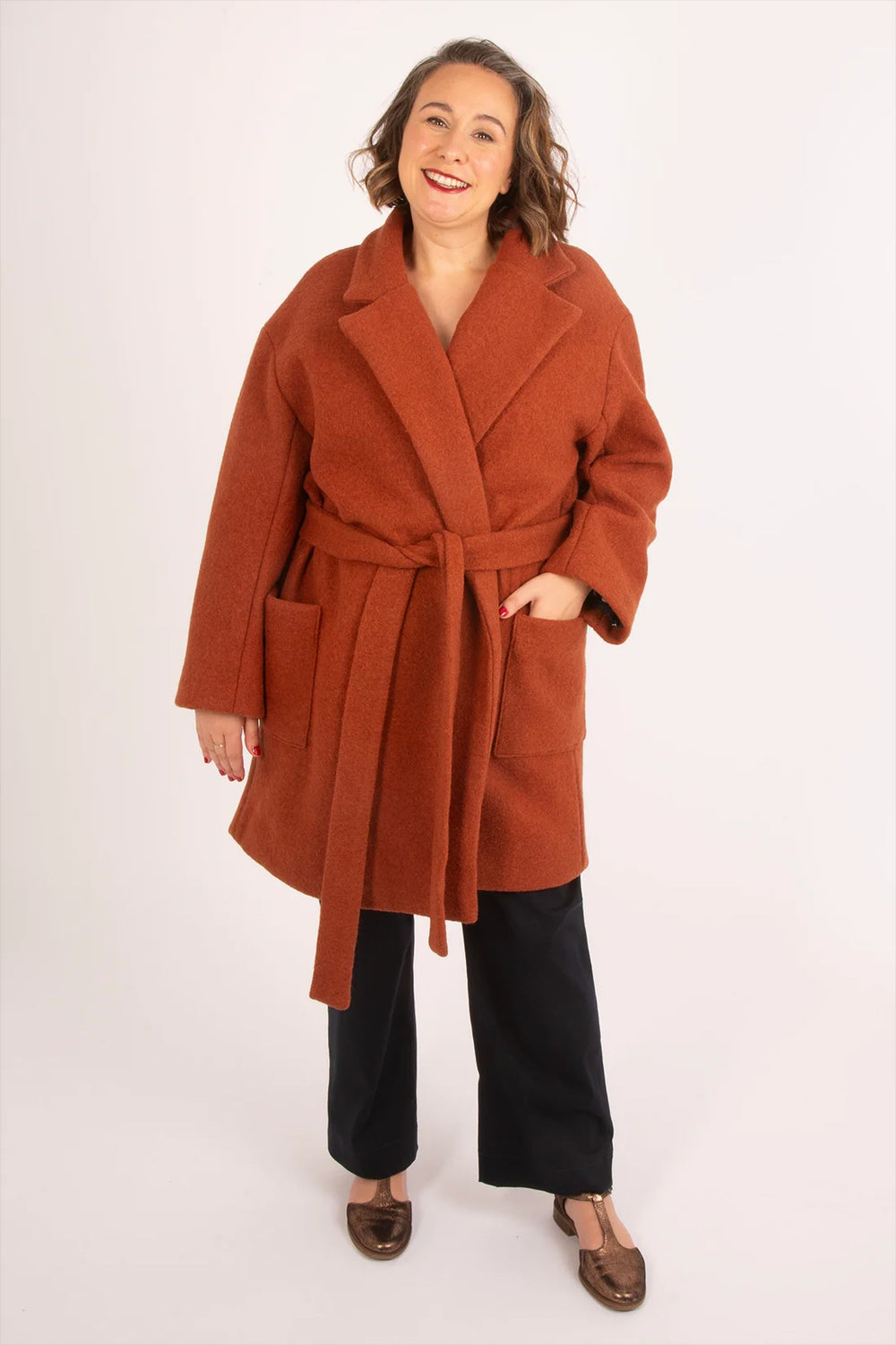 Woman wearing the Opal Coat sewing pattern from Sew Over It on The Fold Line. A fully lined coat pattern made in tweed, boucle, melton, jacquard, or boiled wool fabric, featuring an oversized fit, revere collar with statement lapels, generous wrap with tie belt, and patch pockets.