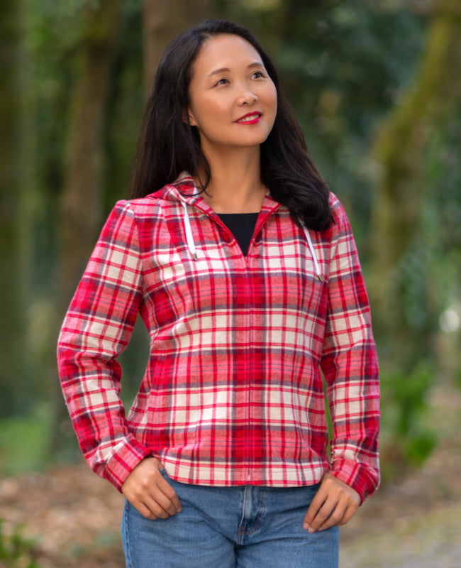 Woman wearing the Orio Jacket sewing pattern from Itch to Stitch on The Fold Line. An unlined jacket pattern made in flannel, brushed cotton, corduroy, linen or linen blend, lightweight denim, chambray, or twill fabric, featuring princess seams, a centre front zip, drawstring hood, two-piece sleeves with plackets and cuffs, single welt pockets, and a shirttail hem.