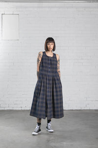 Woman wearing the Page Dress sewing pattern from Elbe Textiles on The Fold Line. A sleeveless dress pattern made in cotton, linen, silk noil, hemp, or linen viscose fabric, featuring a rounded neckline, button front, tucks running down the front and back bodice that open out into a pleated skirt, in-seam pockets, side splits, and midi length.