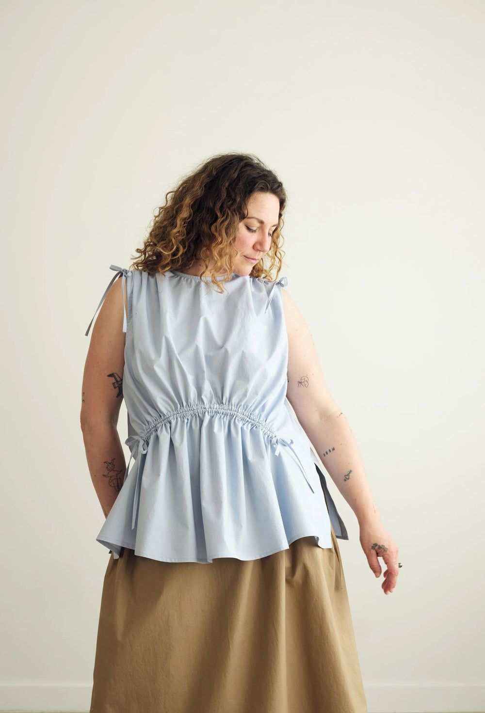 Woman wearing the Paloma Top sewing pattern from the Modern Sewing Co. on The Fold Line. A sleeveless top pattern made in cotton, linen, or tencel blend fabric, featuring a round neckline, channels with ties that create a gathered effect at the shoulders and waist, and side seam splits.