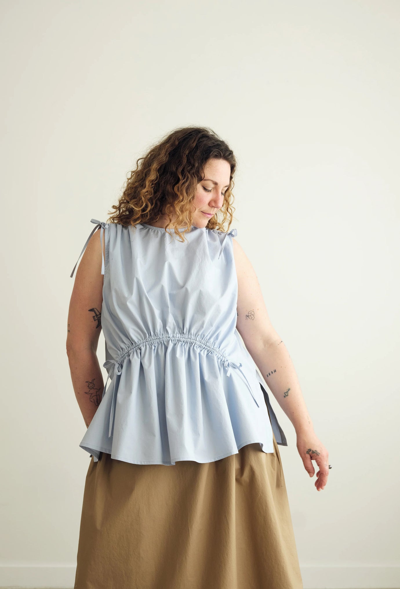 Woman wearing the Paloma Top sewing pattern from the Modern Sewing Co. on The Fold Line. A sleeveless top pattern made in cotton, linen, or tencel blend fabric, featuring a round neckline, channels with ties that create a gathered effect at the shoulders and waist, and side seam splits.