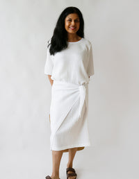 Woman wearing the Pareo Dress sewing pattern from The Maker's Atelier on The Fold Line. A pull-on dress pattern made in cotton, linen, silk, Tana lawn, tencel, viscose, or poly/viscose mix fabric, featuring a round neckline, short sleeves, integrated wrap ties, and midi length.