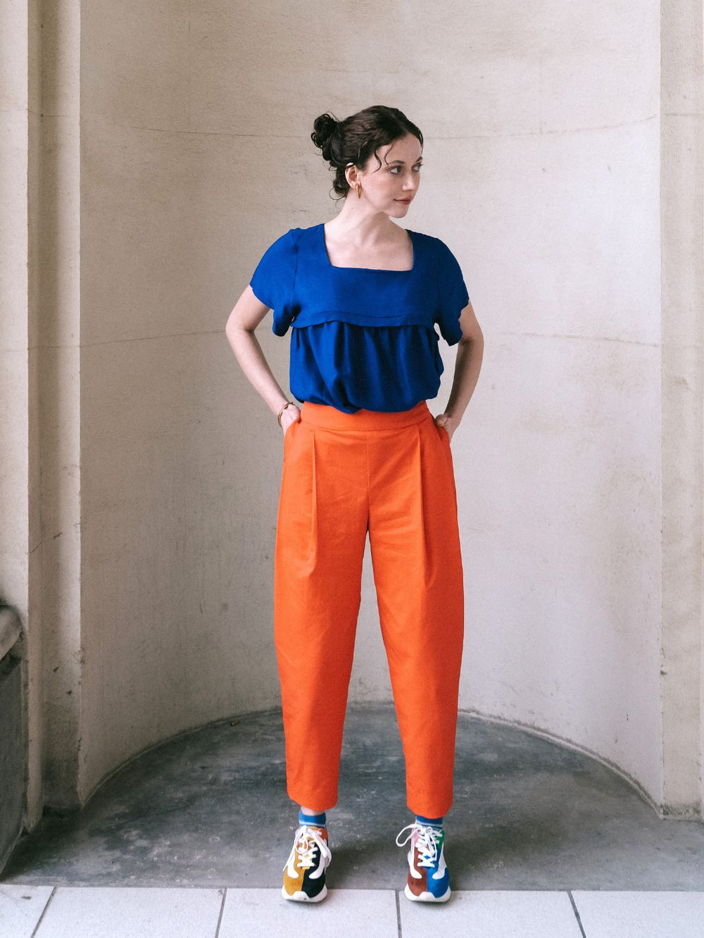 Woman wearing the Paula Trousers sewing pattern from Notches on The Fold Line. A trousers pattern made in thin jacquard, gabardine, seersucker, lyocell denim, heavier viscose, or cupro twill fabric, featuring a high fitted waist with a shaped waistband, front pleats, an invisible side zipper, side pockets, back welt pockets, and tapered legs with darts at the hem.