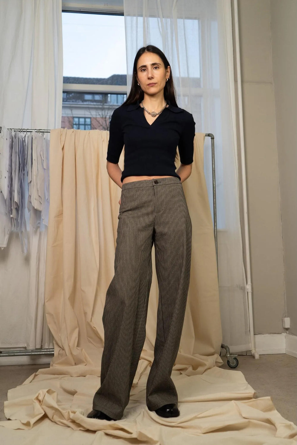 Woman wearing the Peachy Pants sewing pattern from Puff and Pencil on The Fold Line. A trousers pattern made in taslan, denim, linen, lightweight wool, corduroy, or cotton twill fabric, featuring a mid-rise, waistband, fly front zip, back darts, wide slightly curved legs, and patch pockets.