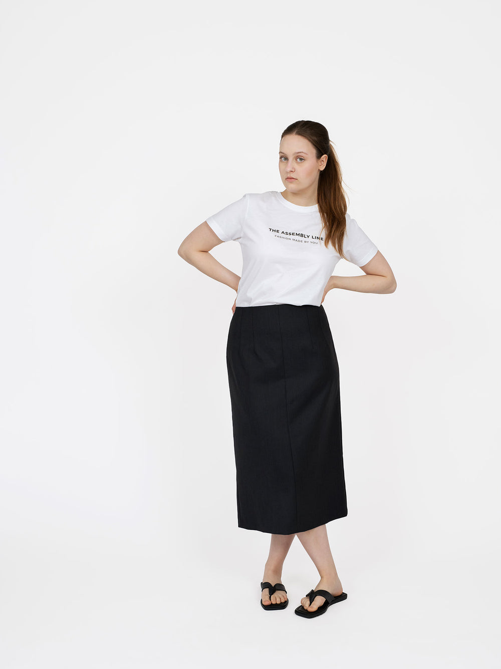 Woman wearing the Pencil Skirt sewing pattern from The Assembly Line on The Fold Line. A skirt pattern made in denim, wool, faux leather, or cotton twill fabric, featuring a fitted silhouette with front and back double darts, back zip, and midi length.