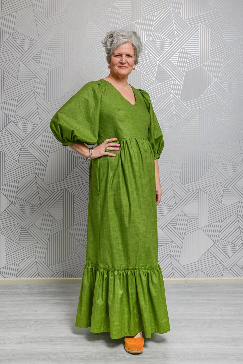 Woman wearing the Penelope Dress sewing pattern from Emporia Patterns on The Fold Line. A dress pattern made in cotton poplin or lawn, viscose lawn, linen, chambray, broderie anglaise, needlecord, crepe, or jacquard fabric, featuring a V-neck, puff  sleeves, and maxi length gathered skirt with pockets and a hem frill.