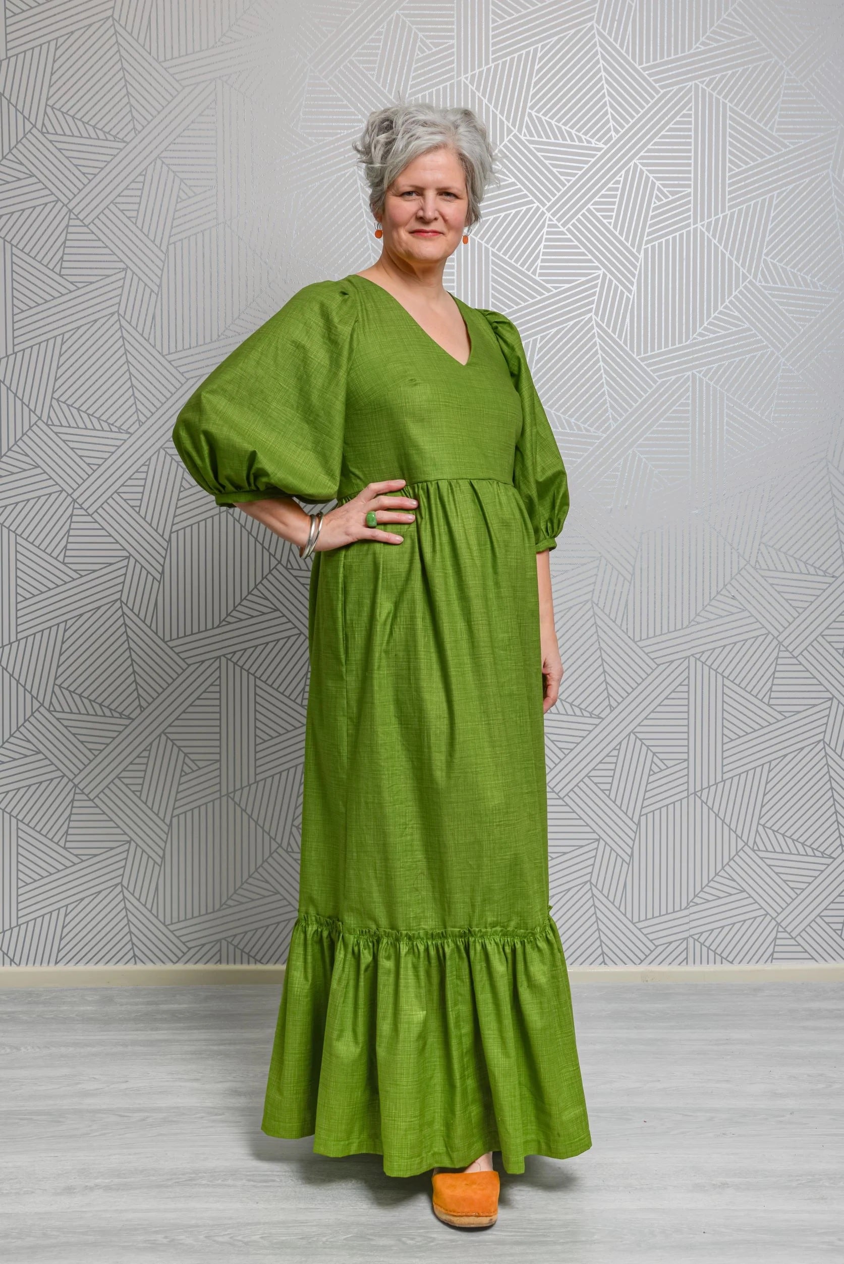 Woman wearing the Penelope Dress sewing pattern from Emporia Patterns on The Fold Line. A dress pattern made in cotton poplin or lawn, viscose lawn, linen, chambray, broderie anglaise, needlecord, crepe, or jacquard fabric, featuring a V-neck, puff  sleeves, and maxi length gathered skirt with pockets and a hem frill.