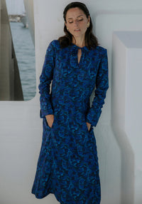 Woman wearing the Péninsule Dress sewing pattern from Maison Fauve on The Fold Line. A dress pattern made in viscose, tencel, cotton, linen, or silk fabric, featuring a lightly fitted shape, round neckline with ties, long sleeves with cuffs, hidden pockets, and a midi length.